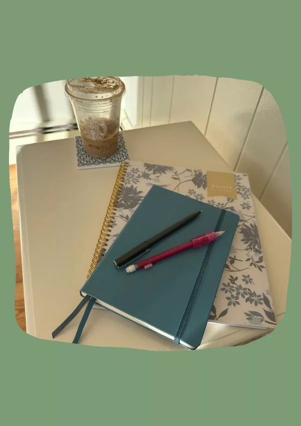 Notebooks, pens, and a drink on a small white table